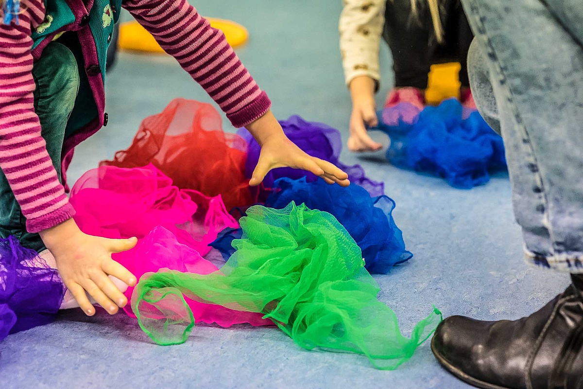 Kinderhände wühlen in einem Haufen bunter Tücher